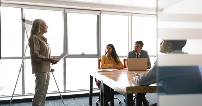 Mature 50s businesslady making flip-chart presentation for staff members
