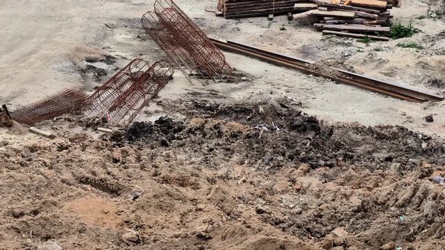 An excavation site reveals visible rebar, massive dirt piles, and scattered construction debris all around