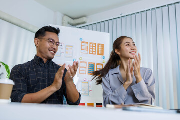 Three people are sitting at a table, working on a project. One of them is holding a piece of paper with a design on it. Scene is collaborative and focused
