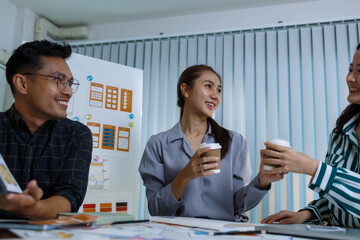 Three people are sitting at a table, working on a project. One of them is holding a piece of paper with a design on it. Scene is collaborative and focused
