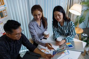 Three people are sitting at a table, working on a project. One of them is holding a piece of paper with a design on it. Scene is collaborative and focused
