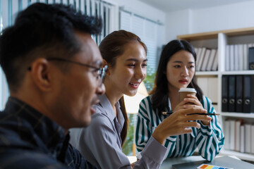 Three people are sitting at a table, working on a project. One of them is holding a piece of paper with a design on it. Scene is collaborative and focused
