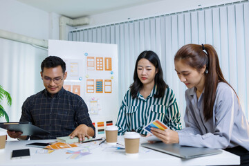 Three people are sitting at a table, working on a project. One of them is holding a piece of paper with a design on it. Scene is collaborative and focused
