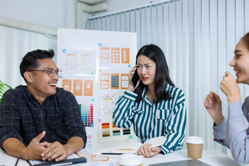 Obraz premium Three people are sitting at a table, working on a project. One of them is holding a piece of paper with a design on it. Scene is collaborative and focused 