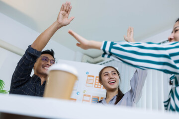 Three people are sitting at a table, working on a project. One of them is holding a piece of paper with a design on it. Scene is collaborative and focused
