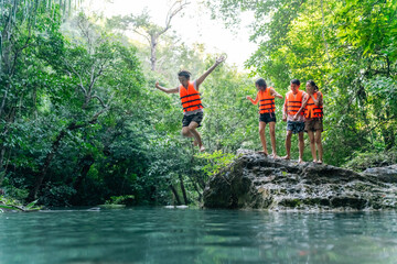 Fototapeta premium Young Asian man and woman travel nature forest hiking and camping on summer holiday vacation. Generation z people friends enjoy and fun active lifestyle playing water in waterfall lagoon in sunny day.