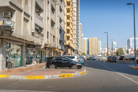 Busy commercial street with shops, old apartments, and parked cars near Hamdan Street, Abu Dhabi, UAE, with distant skyscrapers on a sunny day
