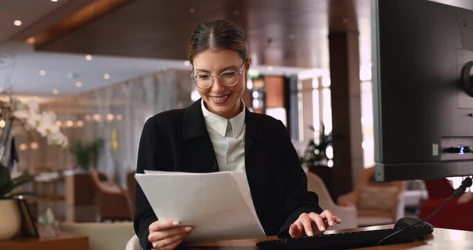 Female hotel receptionist managing documents and computer tasks