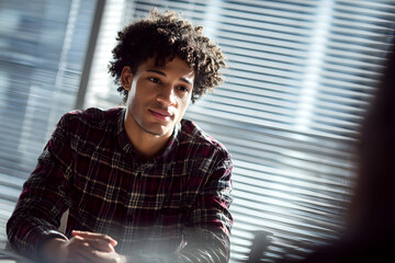 Young man in plaid shirt sitting in front of window blinds. Business concept