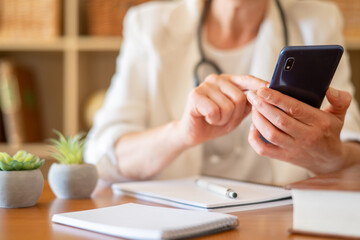 Fototapeta premium Healthcare professional using a smartphone at a desk, offering virtual medical consultation and managing appointments, representing modern technology in healthcare