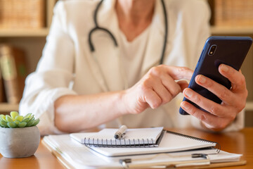 Healthcare professional holding and interacting with a smartphone, providing remote telehealth services and virtual doctor visits from a modern clinic or office environment