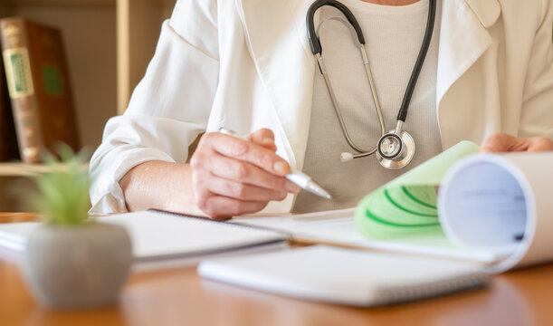 General practitioner wearing a stethoscope and white coat, holding a pen and reviewing patient files, focusing on healthcare consultation and primary care