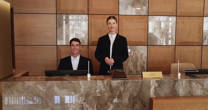 Two hotel receptionists stand behind front desk in hotel lobby