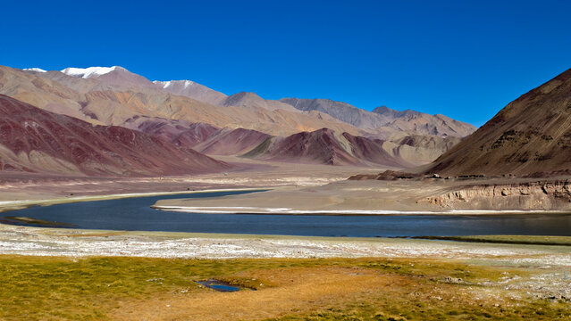 Winding dirt road to Hanle at 4,500m in Ladakh, flanked by rugged valleys and snow-capped peaks under blue skies, captured September 2025. Epitome of high-altitude adventure and remote wilderness.