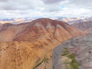 Close aerial view of sharply eroded, richly colored red and orange mountain slopes with a winding river valley below