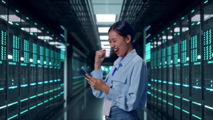 Side View Of Asian Female Professional Worker With Her Smartphone In Server Room Data Center, She Raises Her Fist Up With Screaming Goal After Check On The Smartphone - Powered by Adobe