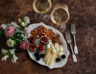 Aperitif table - two glasses of white wine and a plate of appetizers on a wooden table, top view