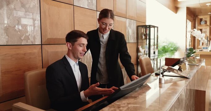 Two receptionists using computer, working together at reception desk