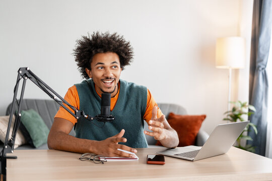 Smiling man recording podcast talking into microphone at home