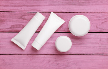 White cream tubes and jars on pink wooden background. Template for design. Beauty concept
