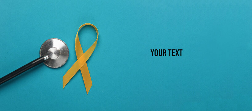 Yellow ribbon, childhood cancer awareness day symbol and stethoscope on blue background. Copy space for your text