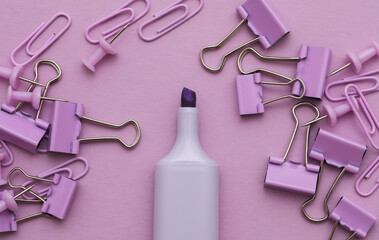 Stationery set of purple paper clips, binders, pins with marker on purple background. School supplies