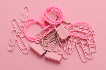Stationery set of pink paper clips, binders, pins and rubber bands on pink background. Creative layout