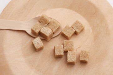 Cubes of cane brown sugar in wooden plate on white background. Eco concept