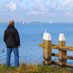 Man stands on the shore of a lake and looks into the distance at white yachts