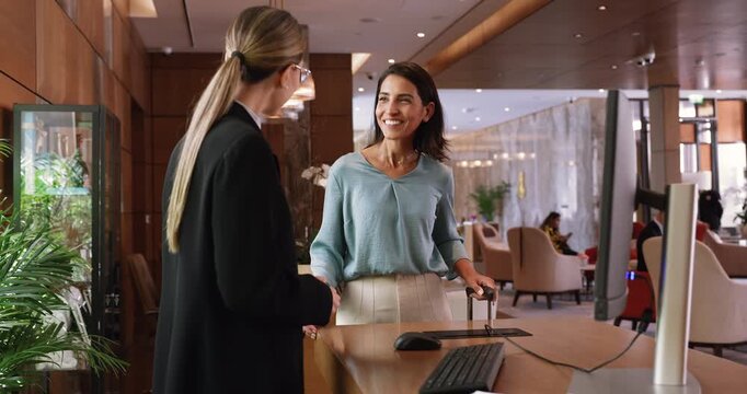 Smiling female hotel guest arrives at front desk with luggage