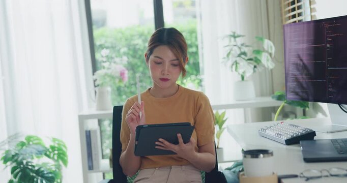 Young adult Asia female freelance write code on tablet while work prompt AI bot IT app smart program nomad, video game, terminal coding, user interface, data center on desktop computer at home office.