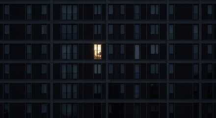 Building exterior at dusk many dark windows one apartment brightly lit with warm interior light