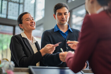 Guests filling registration form during hotel check-in process and pay with credit card with receptionist in uniform. Concept of travel payment, vacation, and customer satisfaction.