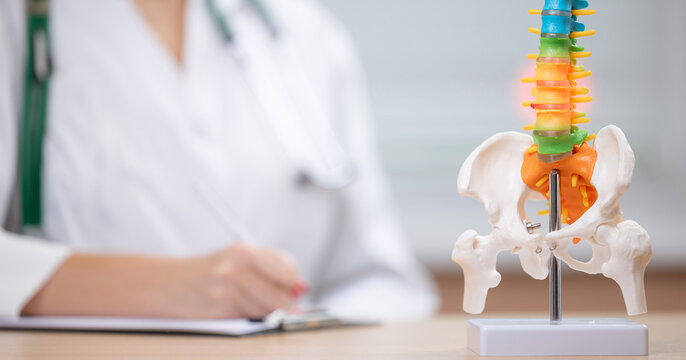 Doctor orthopedist in white coat examines spine model with glowing areas indicating pain or issues