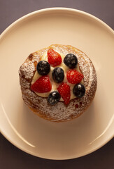 A pastry topped with fresh strawberries, blueberries, and rich cream, elegantly served on a white plate
