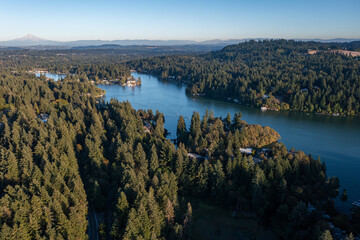 Aerial drone picture of Lake Oswego, Oregon and Mount Hood in backgrond, showing calm blue water surrounded by dense forest and residential houses, real estate, on a clear sunny evening at sunset.  
