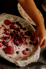Hand adding frozen berries on creamy yogurt dessert