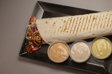 A delicious grilled wrap served with three flavorful dipping sauces and a healthy side of fresh vegetables