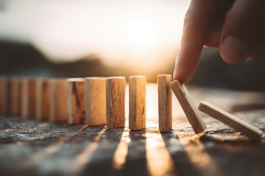 A hand pushes a domino, initiating a chain reaction