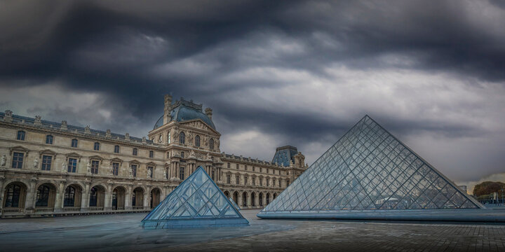 Paris, France - October 04 2025: Striking glass pyramids at Paris Louvre under a dramatic sky.
