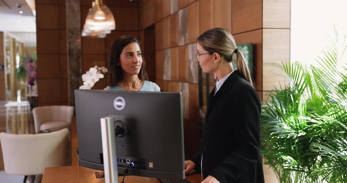Hotel receptionist showing information on computer screen to female guest