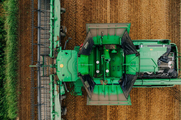 Aerial view of a green combine harvester working in a field with visible rows of harvested and...