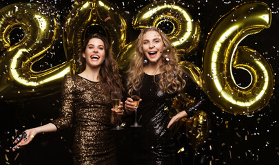Two young ladies drinking champagne. Image of girls with balloons isolated on black background, having fun at New Year's 2021 Eve Party.