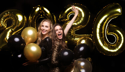 Happy gorgeous girls in stylish sexy party dresses holding gold 2026 balloons, having fun at New Year's Eve Party.