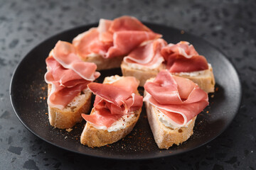 bruschetta with prosciutto and cream cheese on black plate on conctere background