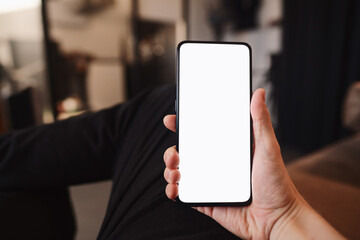 Man hold smartphone with white screen in his hand sitting on a couch in home environment