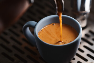 Closeup espresso pour with single spout portafilter in blue cup