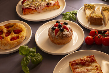 Various baked goods, delicious pastries, and ripe fresh tomatoes are beautifully arranged on plates, adorned with basil