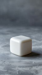 A single white bar of soap sits on a textured gray surface with soft lighting