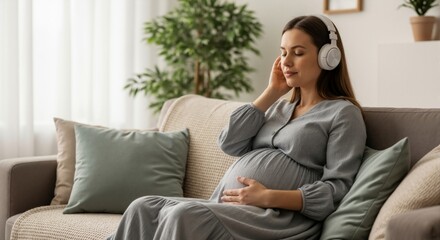 Pregnant woman with headphones relaxing on a sofa and listening to music. Expectant mother touching her belly at home. Prenatal wellness concept